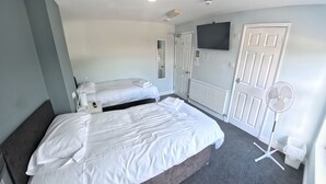 Ein Hotelzimmer mit zwei Betten, einem Fernseher, einem Ventilator und einer Heizung.