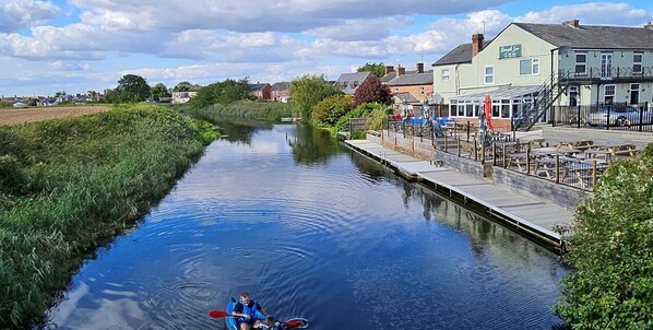 A narrow canal with a row of buildings on one side and a grassy bank on the other. - Riverside Inn (Spalding)