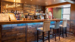 Eine Bar mit Holzwänden, einer Neonreklame mit der Aufschrift "Riverside Inn" und einer Auswahl an Spirituosenflaschen.