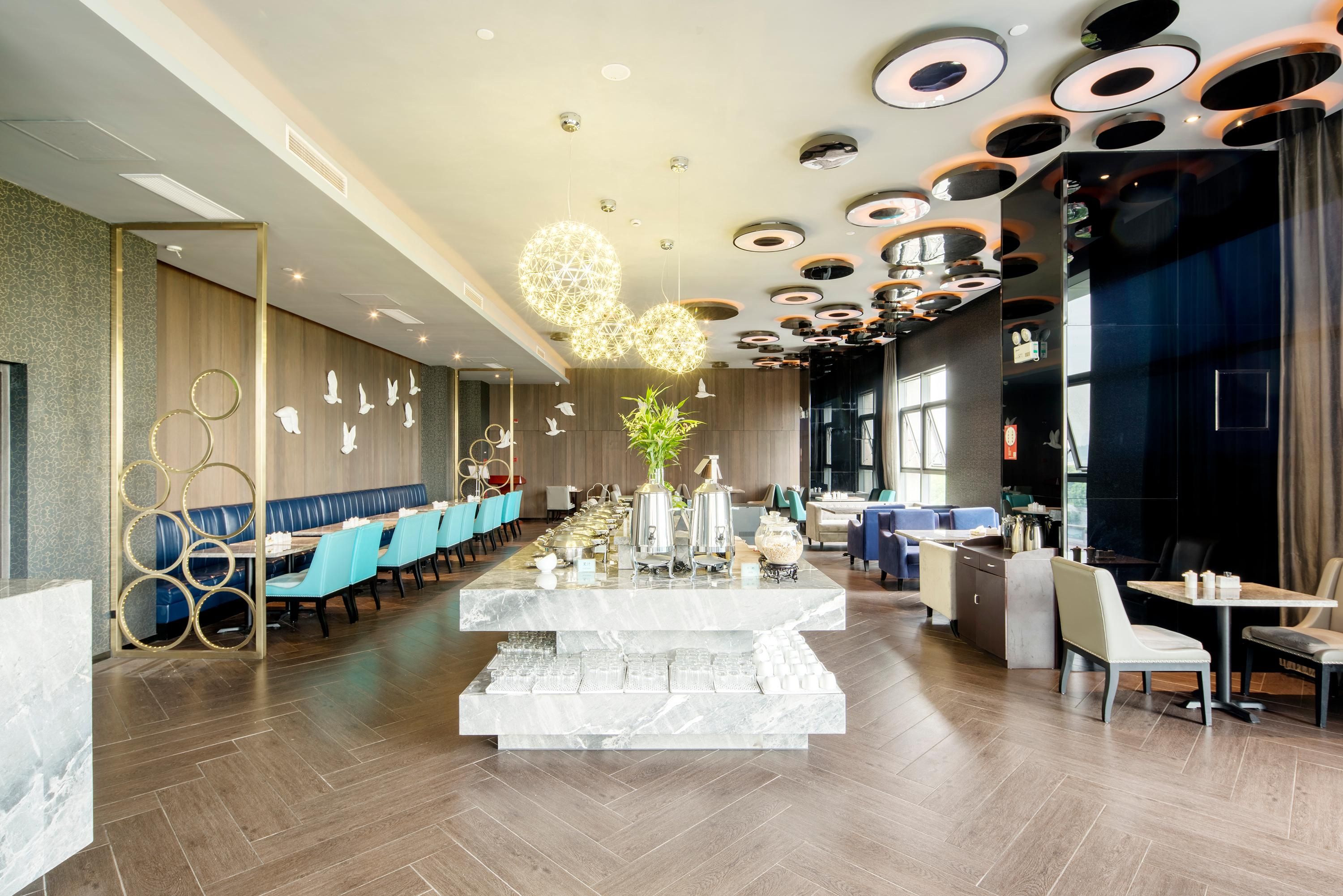 A modern restaurant interior with a central marble bar, blue seating, and a unique ceiling design.