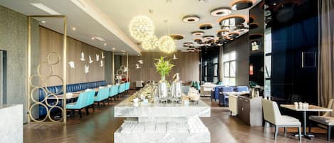 A modern restaurant interior with a central marble bar, blue seating, and a unique ceiling design.
