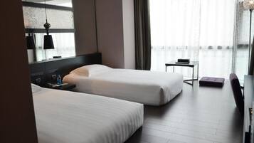 Habitación de hotel con dos camas, una mesita, una silla y un ventanal grande con cortinas.