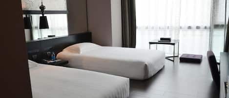 Habitación de hotel con dos camas, una mesita, una silla y un ventanal grande con cortinas.