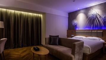 Una habitación de hotel moderna con una cama grande, un sofá, una mesita y una lámpara fijada a la pared.