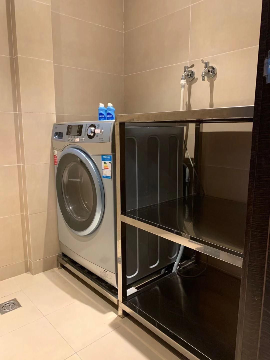 Un lavadero pequeño con lavadora de carga frontal, un estante y un calentador de agua.