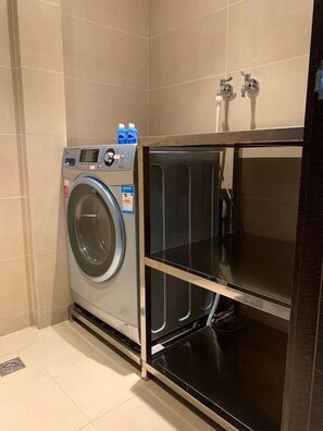 A compact laundry room with a front-loading washing machine, a shelf unit, and a water heater. - Crystal Orange Hotel Changzhou Dinosaurs Park (Changzhou)