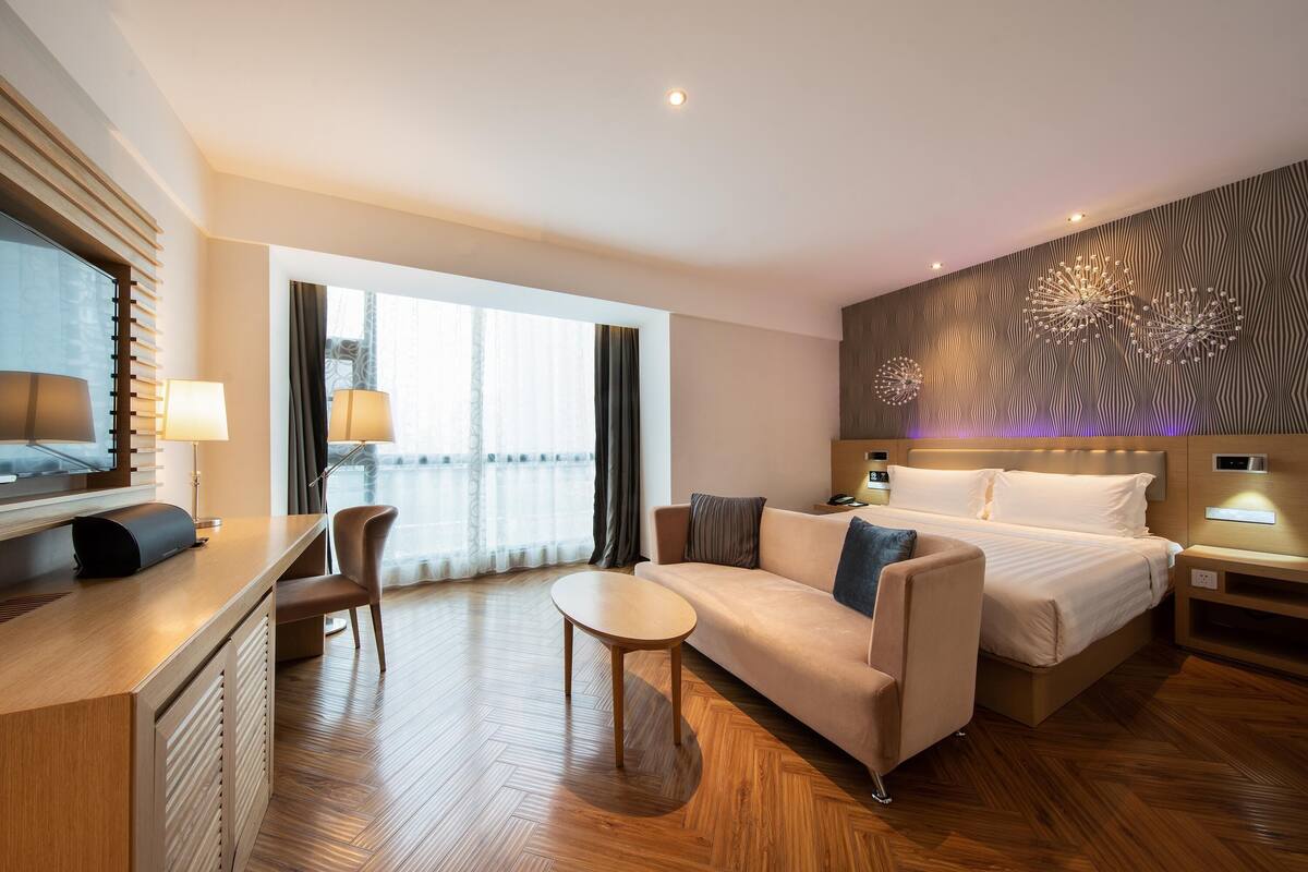 Ein modernes Hotelzimmer mit Bett, Sofa, Schreibtisch und einem großen Fenster.