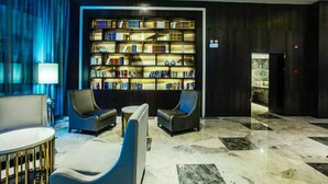 A modern lobby with a large, illuminated bookshelf, comfortable seating, and a marble floor.