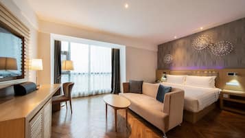 A modern hotel room with a bed, sofa, desk, and a large window.
