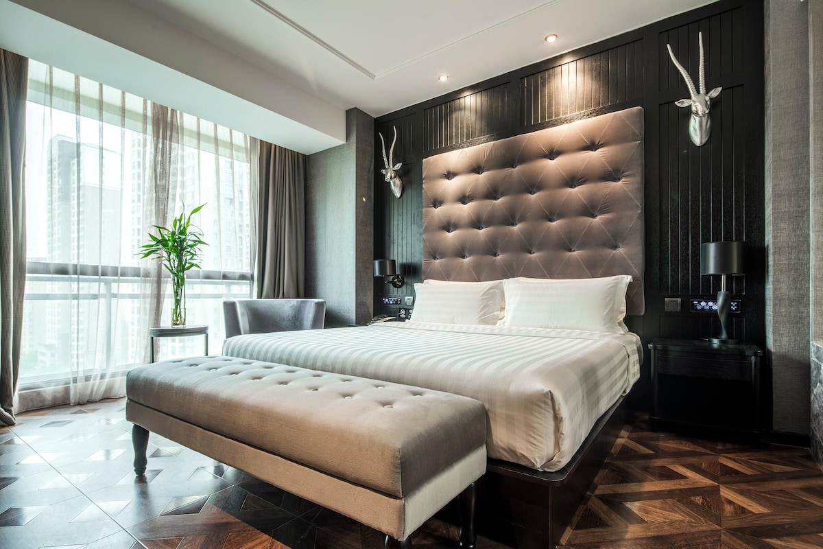 Une chambre à coucher moderne avec un grand lit, un banc, une table de chevet et une tête d’animal fixée au mur.