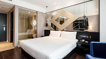 A modern hotel room with a large bed, a desk with a lamp, and a mirror with geometric patterns.