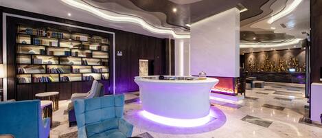 A modern lobby with a central reception desk, a bookshelf, and seating areas.