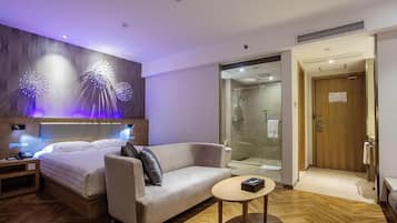 Una habitación de hotel moderna con cama, sofá, una mesita y zona de ducha.