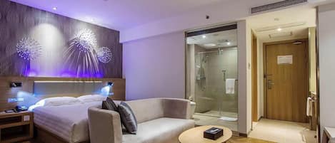 Una habitación de hotel moderna con cama, sofá, una mesita y zona de ducha.