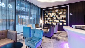 A modern hotel lobby with a large bookshelf, comfortable seating, and a reception desk.