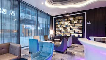 Un moderno vestíbulo de hotel con un área de descanso, una recepción y una estantería llena de libros.