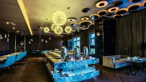 A modern restaurant with a marble bar, blue chairs, and a unique ceiling design.