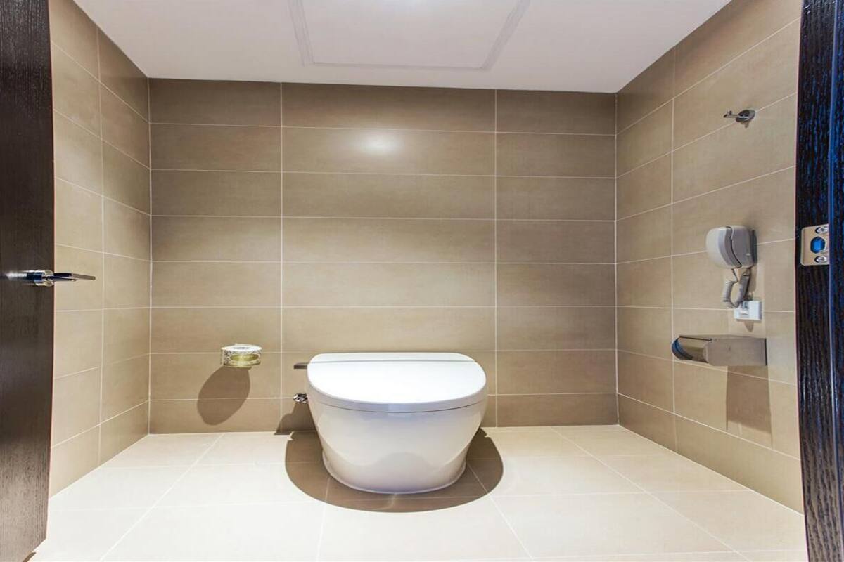 Ein modernes Badezimmer mit Toilette, einem Handtrockner und einem Seifenspender an der Wand.