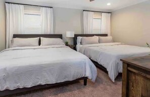 Two single beds with wooden headboards and white bedding, a nightstand with a lamp, and a window with white curtains.
