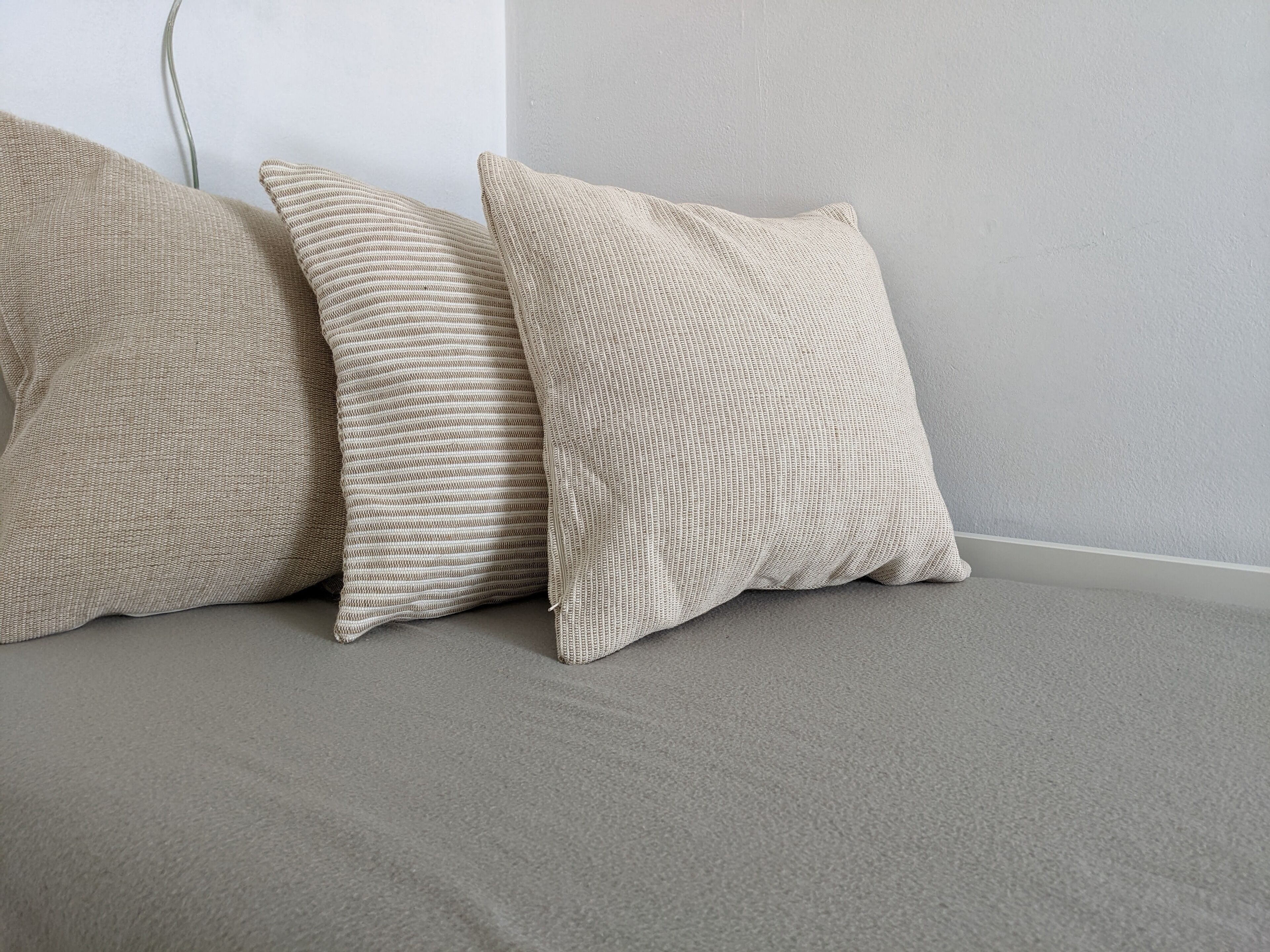 Three textured pillows on a grey sofa against a plain wall.
