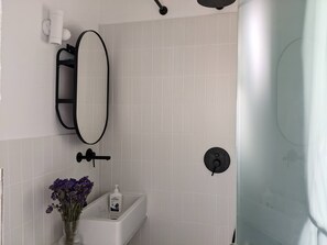 Un baño con un lavamanos blanco, un espejo, un toallero negro y una zona de ducha.
