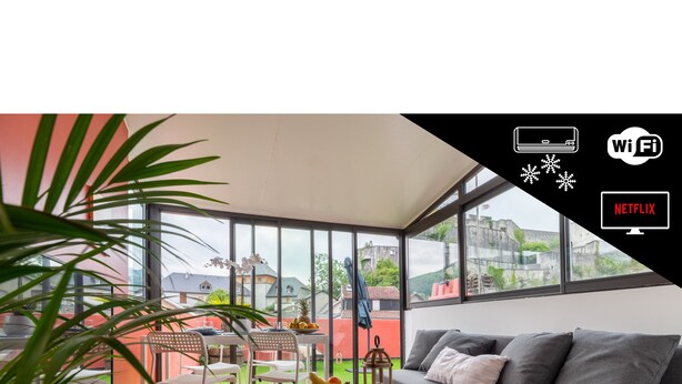Ein modernes Wohnzimmer mit einem grauen Sofa, einem weißen Couchtisch und Blick auf ein rotes Gebäude durch große Fenster.