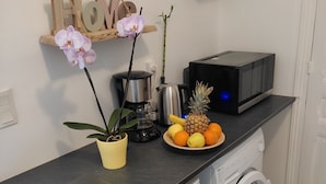 Eine kompakte Küche mit Waschmaschine, Kaffeemaschine, Mikrowelle und einem kleinen Regal mit Dekoration.