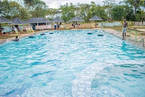 Piscina con sillas de descanso y sombrillas, rodeada de árboles.