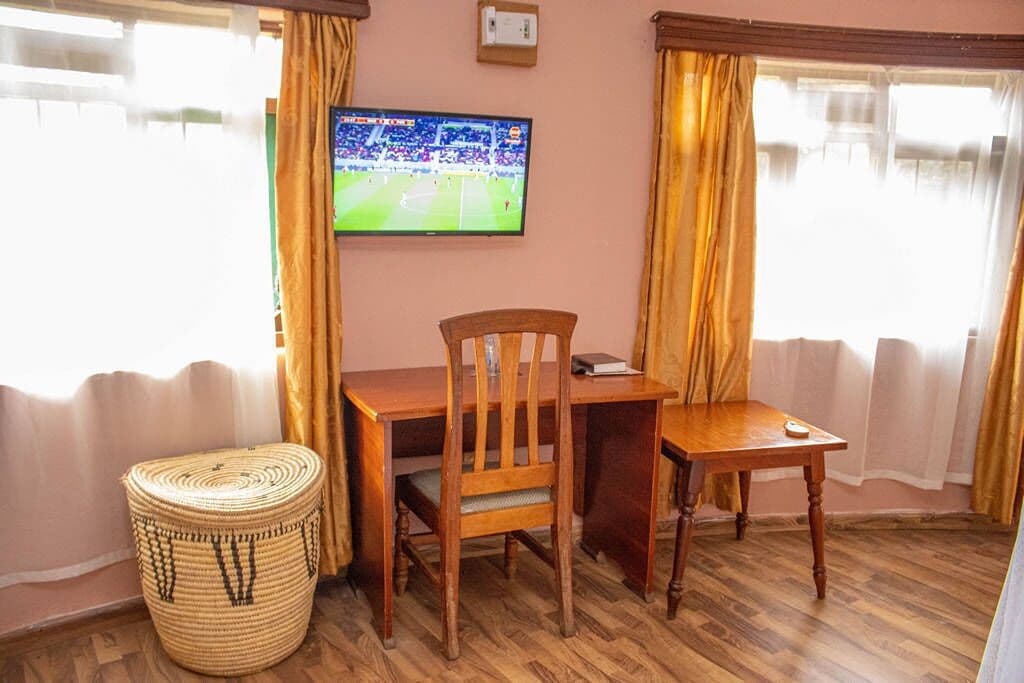 A room with a wooden desk, two chairs, a television mounted on the wall, and a woven basket on the floor.