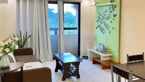 A modern living room with a dining area, large windows, a ceiling fan, and a green wall with floral art. - Spacious Condo 1BR with Washer near SM Mall (Davao City)