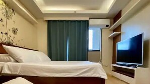A modern hotel room with a bed, a TV, and a window with curtains. - Spacious Condo 1BR with Washer near SM Mall (Davao City)