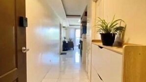 A hallway with a welcome mat, a potted plant, and a door on the left. - Spacious Condo 1BR with Washer near SM Mall (Davao City)