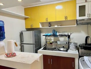 A compact kitchen with yellow cabinets, a stainless steel refrigerator, a sink with a kettle, and a stove. - Spacious Condo 1BR with Washer near SM Mall (Davao City)