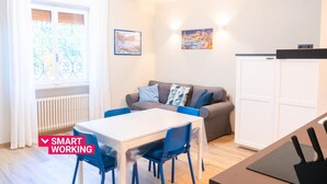 A modern living room with a white table, blue chairs, a grey sofa with patterned cushions, and a white cabinet. - Lemon Apartment With Garden and Sea View by Wonderful Italy (Bordighera)