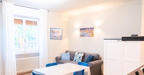 A modern living room with a white table, blue chairs, a grey sofa with patterned cushions, and a white cabinet. - Lemon Apartment With Garden and Sea View by Wonderful Italy (Bordighera)