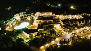 En vy från ovan av ett hotell med flera våningar, en swimmingpool, flera balkonger och ett väl upplyst utomhusområde.