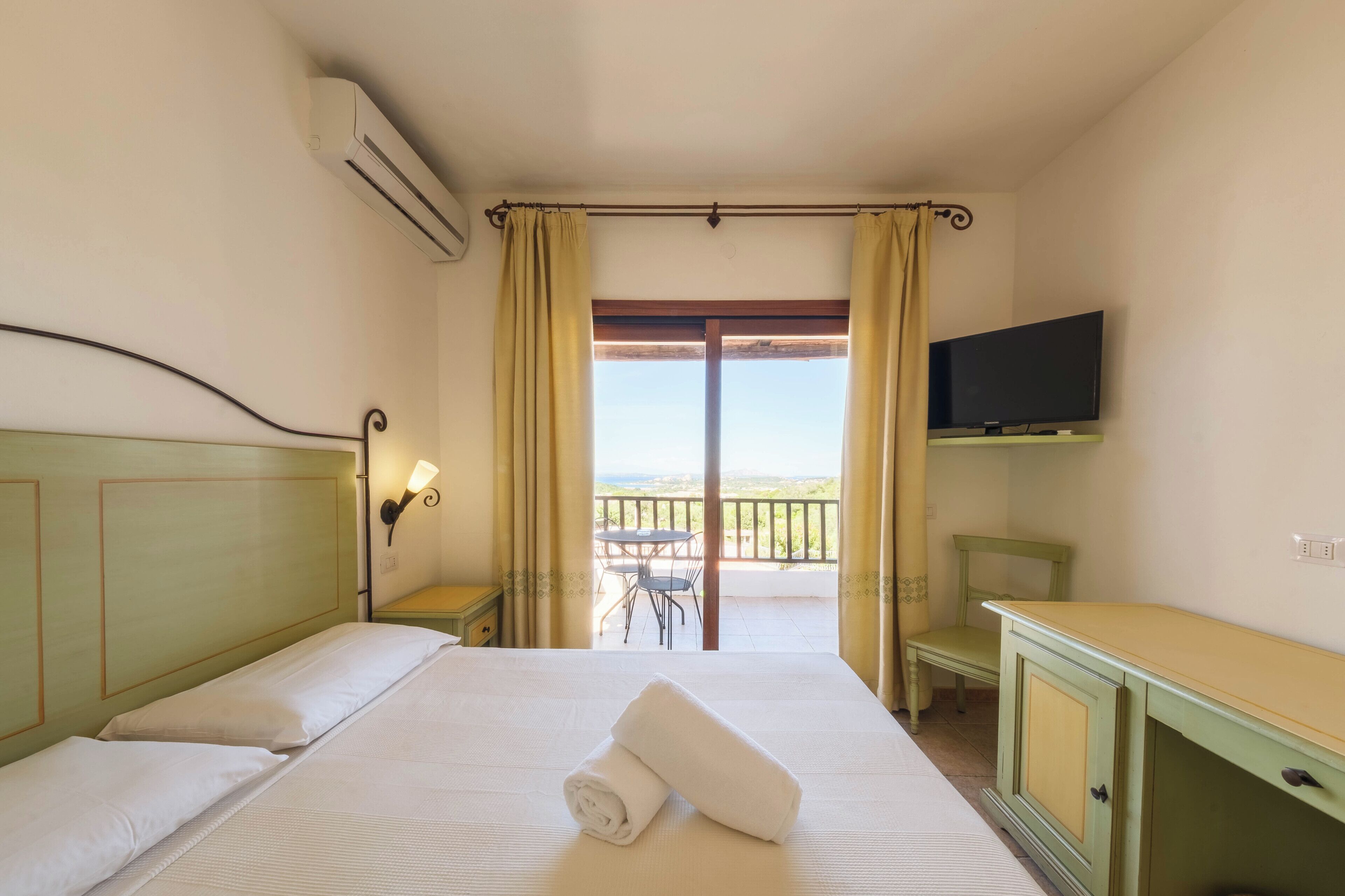 A hotel room with a bed, a television, a desk, and a balcony with a table and chairs.