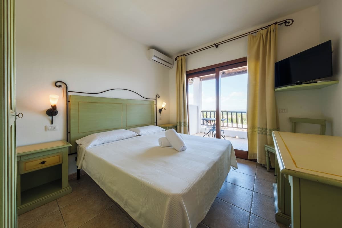 A hotel room with a bed, bedside tables, a TV, and a balcony with curtains.