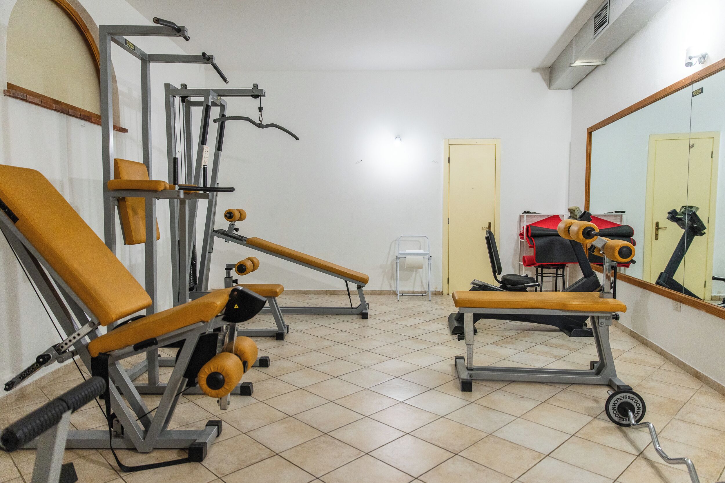 A gym with exercise equipment, a bench, and a mirror on the wall.