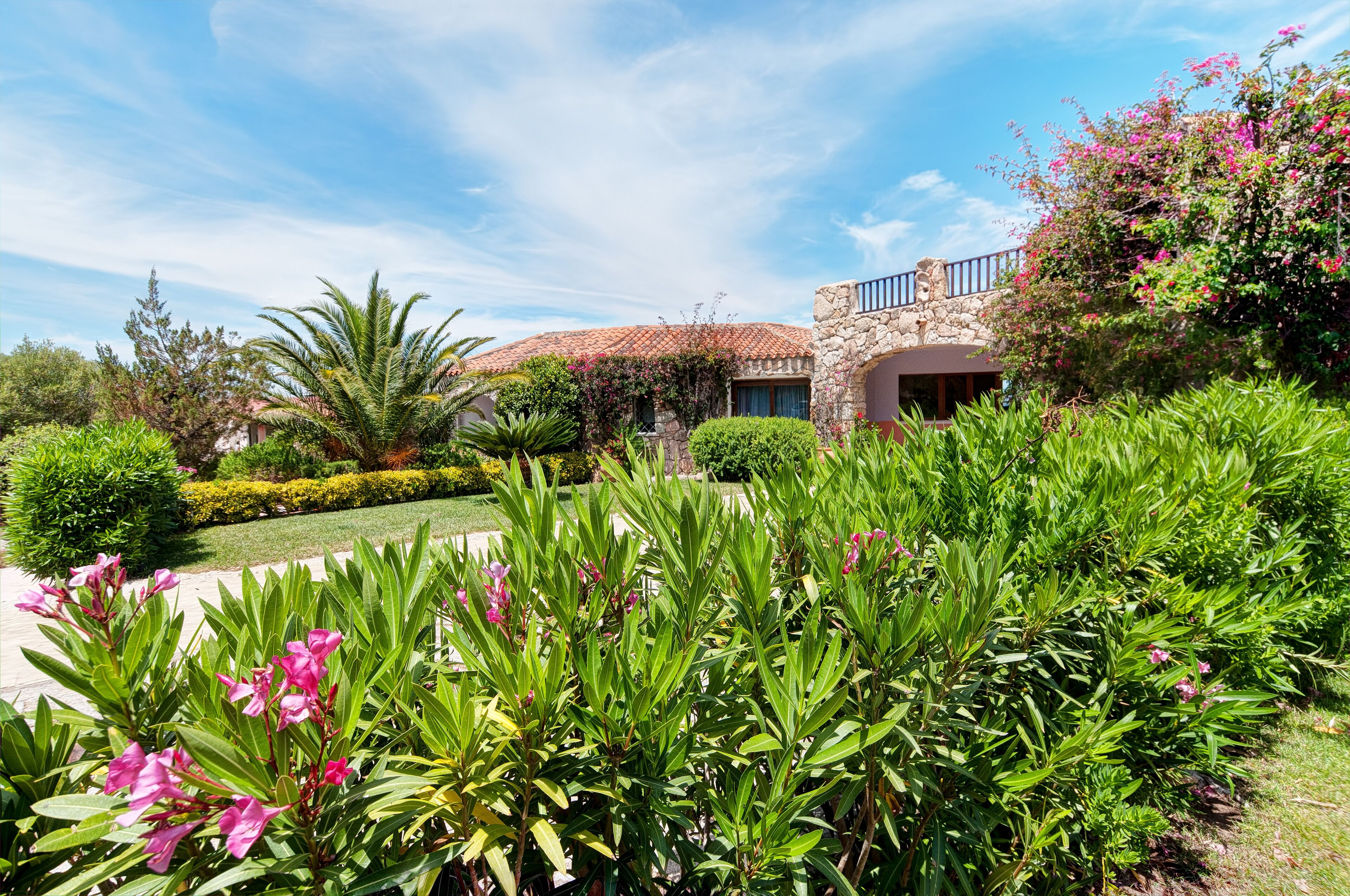 A stone building with a tiled roof, surrounded by lush greenery and flowering plants.