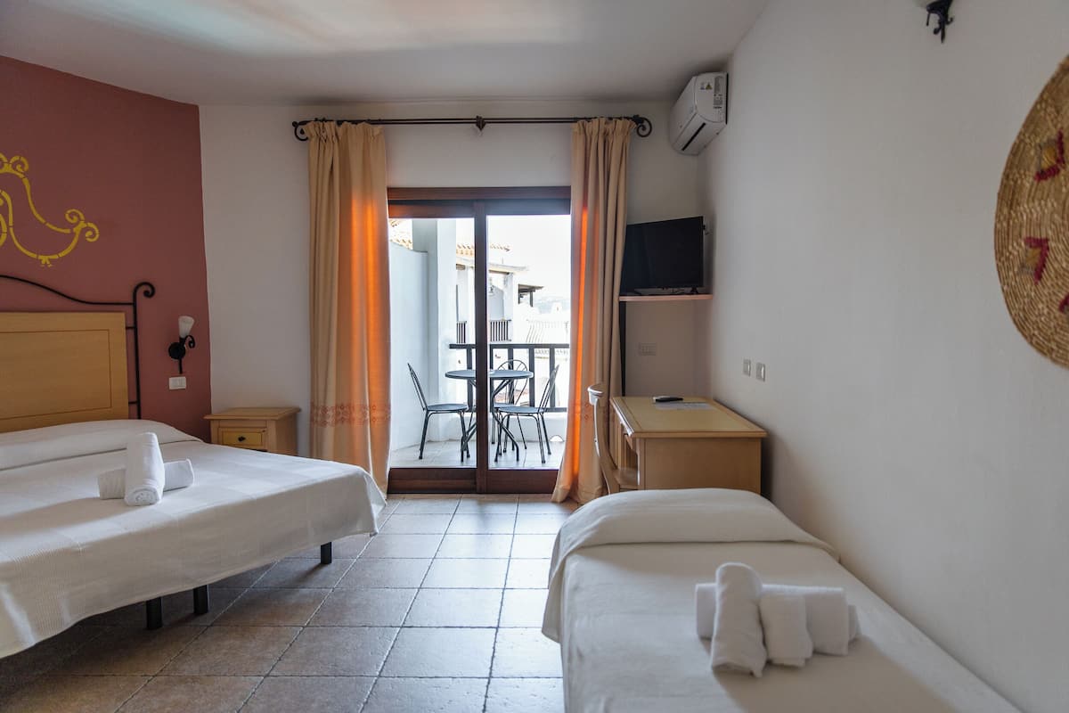 A hotel room with two beds, a TV, a desk, and a balcony with chairs.