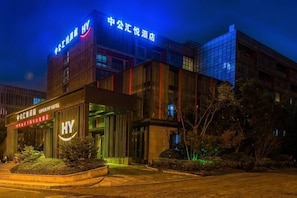 Ein Hotel mit modernem Design, das ein auffälliges 'HY'-Schild, einen gut beleuchteten Eingang und eine stufenartige Fassade zeigt.