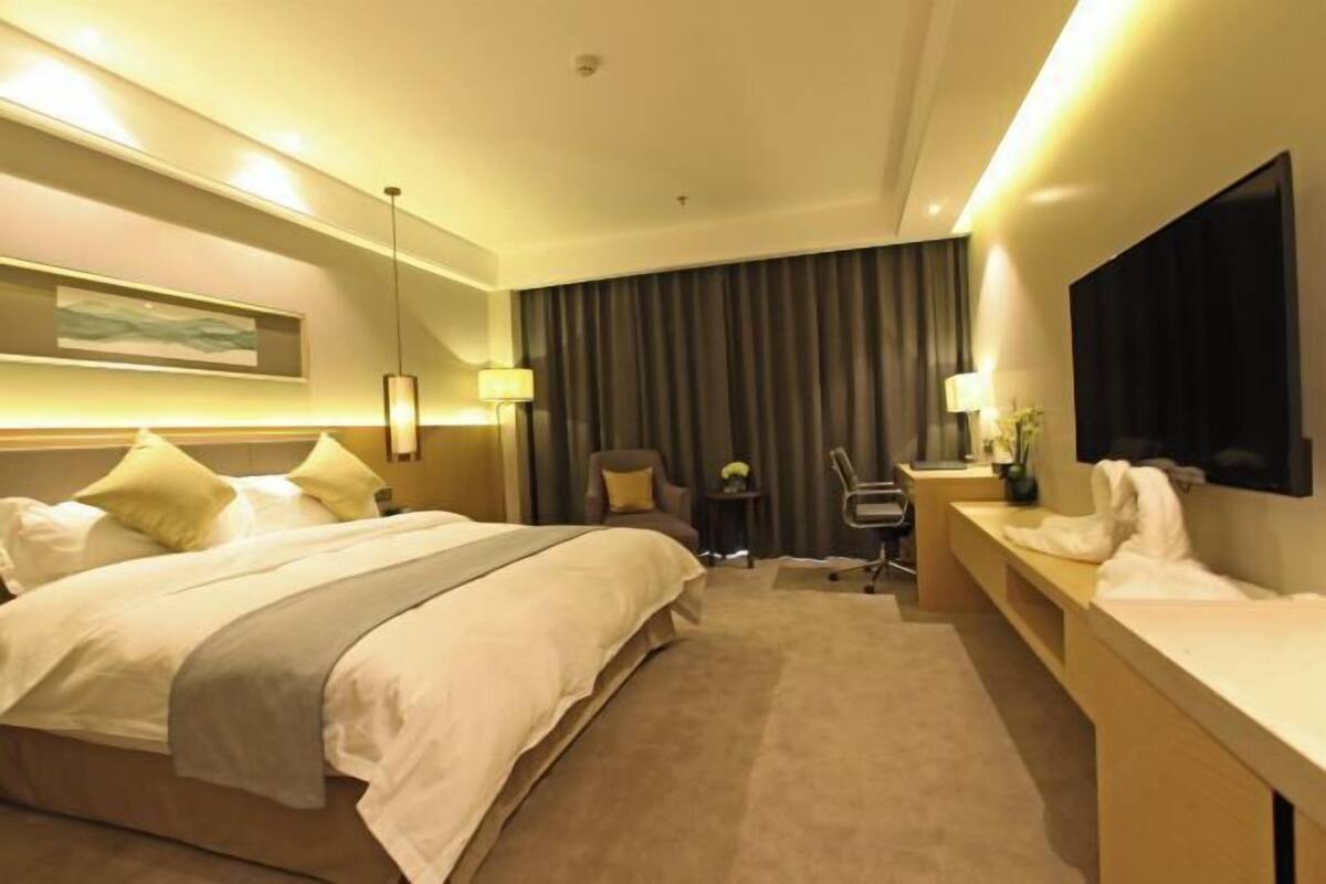 A hotel room with a large bed, a desk, a chair, a TV, and a window with curtains.