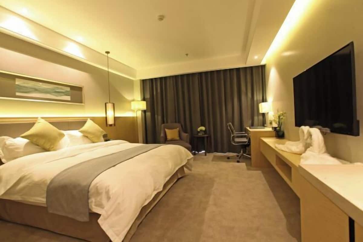 A hotel room with a large bed, a desk, a chair, a TV, and a painting on the wall.