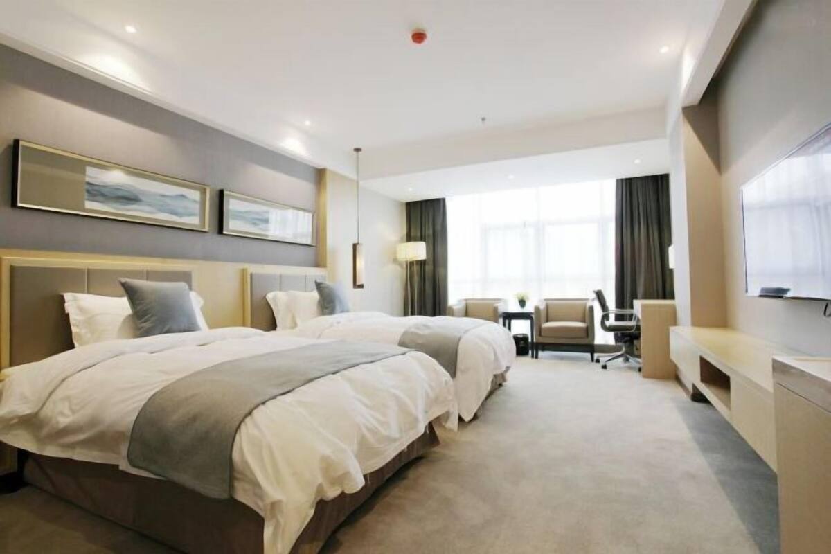 A hotel room with two beds, a desk, a chair, and a TV.