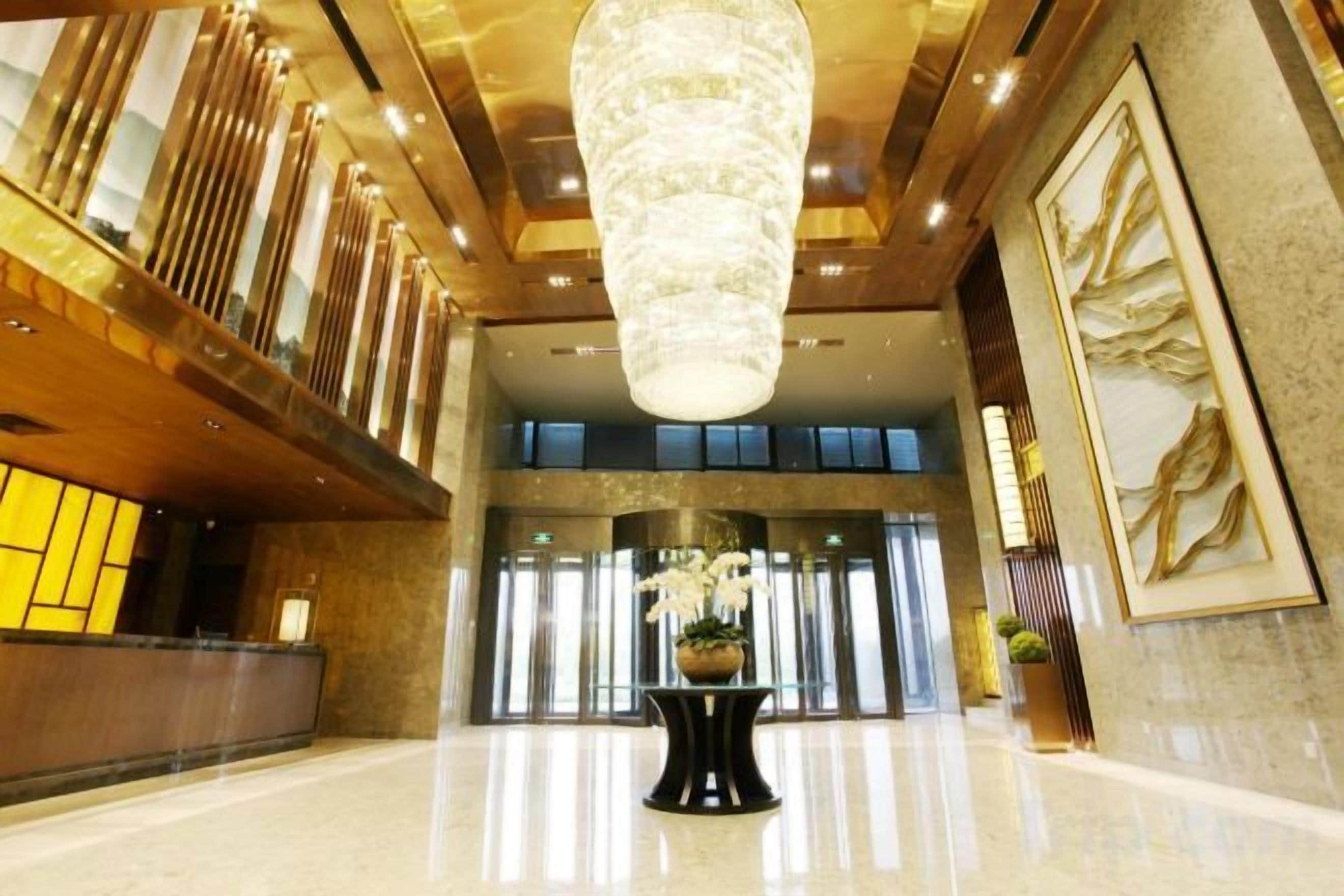 A spacious lobby with a high ceiling, a central chandelier, and a reception desk.