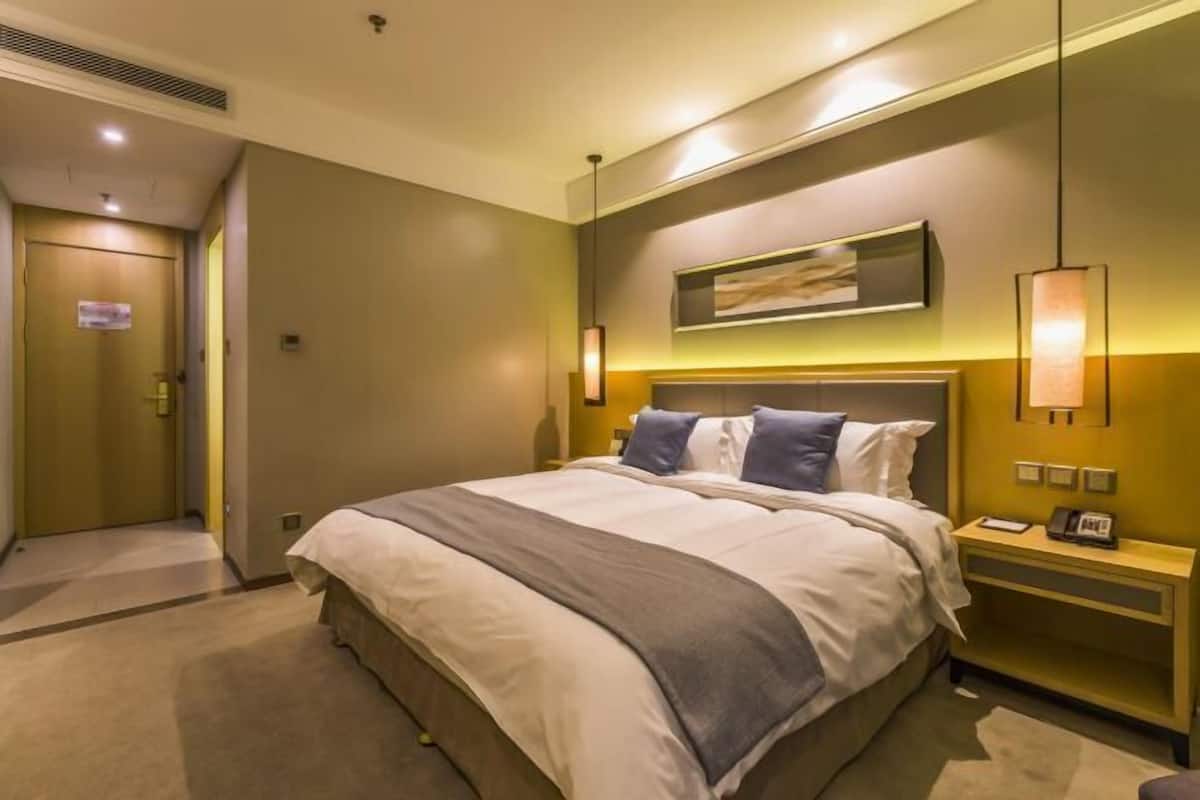 A hotel room with a large bed, bedside tables, a wall-mounted artwork, and a door to the left.