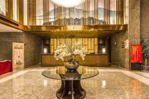 A lobby with a reception desk, a glass-top table with a vase of flowers, and a mural on the wall. - OffCN HY Hotel (Nanjing)