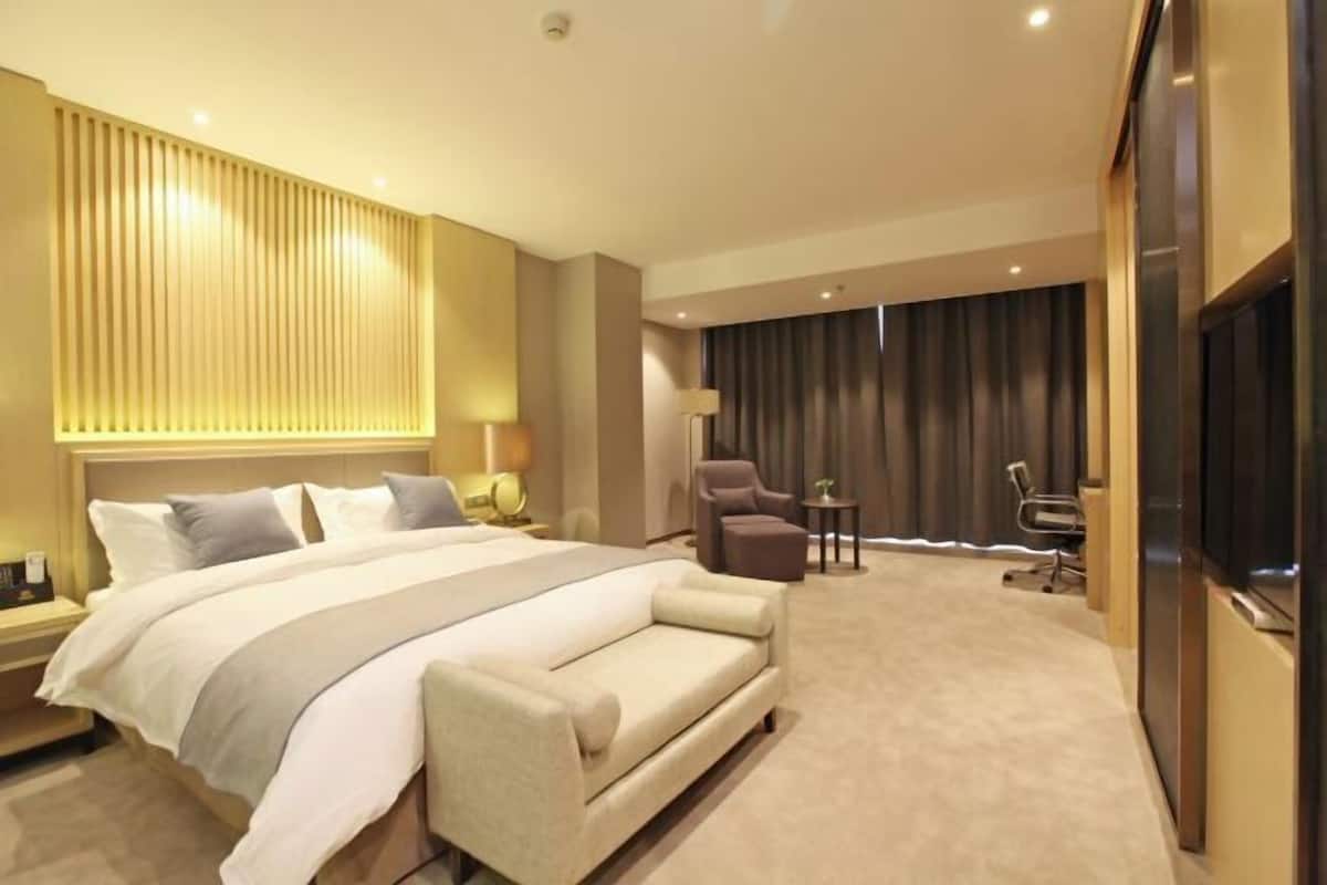 A hotel room with a large bed, a sofa, a desk, and a chair.