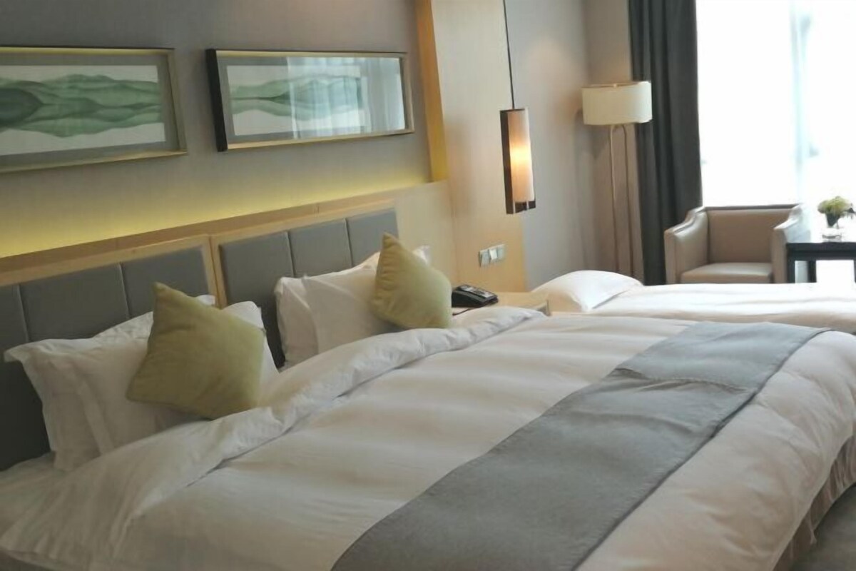 A hotel room with two beds, a headboard, a lamp, and a chair.